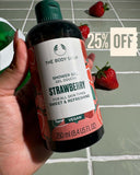 The Body Shop Strawberry shower gel held by a hand with strawberries in the background